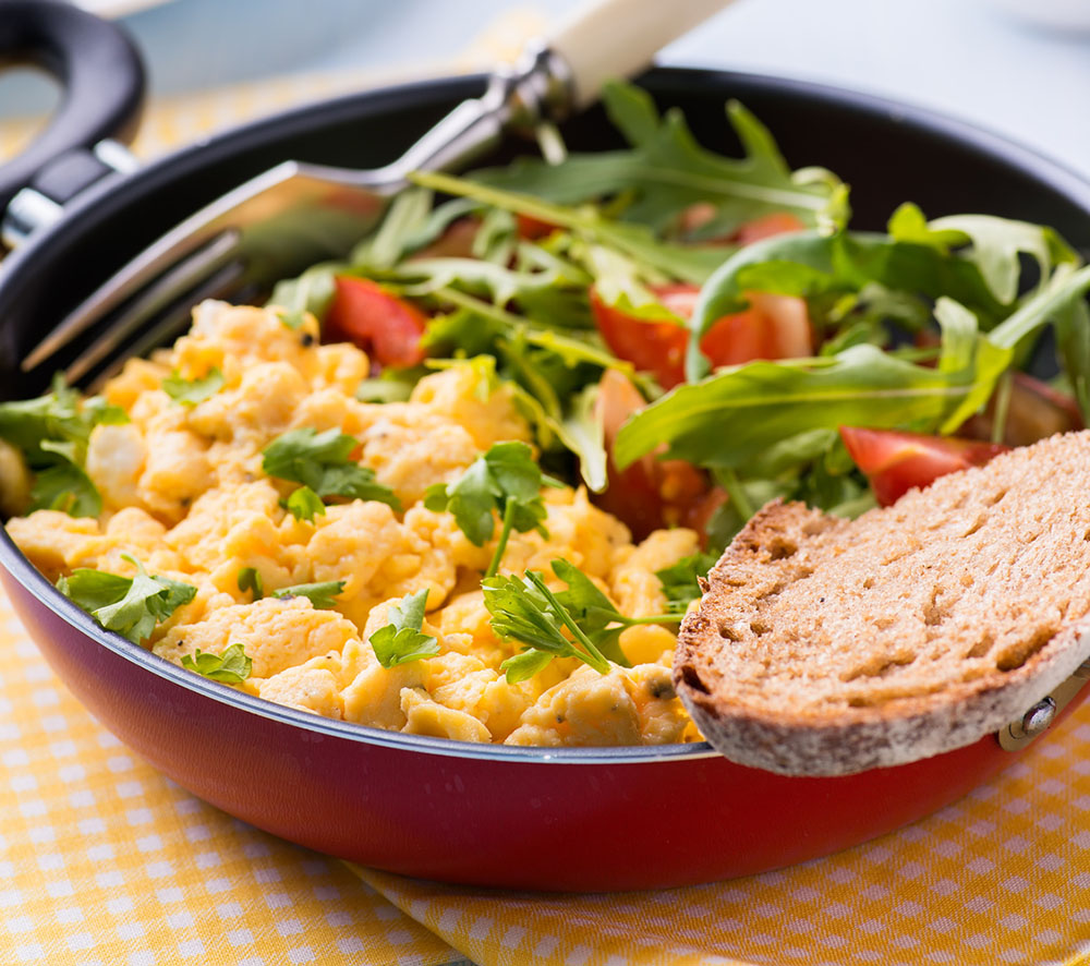 Scrambled eggs with fresh tomato and arugula salad in frying pan