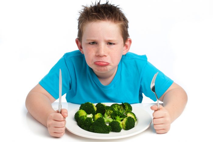 A young boy who is not happy about eating his broccoli.