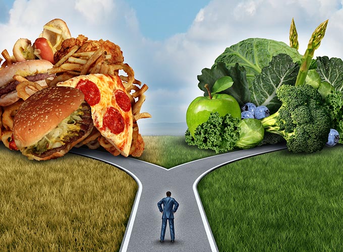 Diet decision concept and nutrition choices dilemma between healthy good fresh fruit and vegetables or greasy cholesterol rich fast food. Man on a crossroad trying to decide what to eat for the best lifestyle choice.